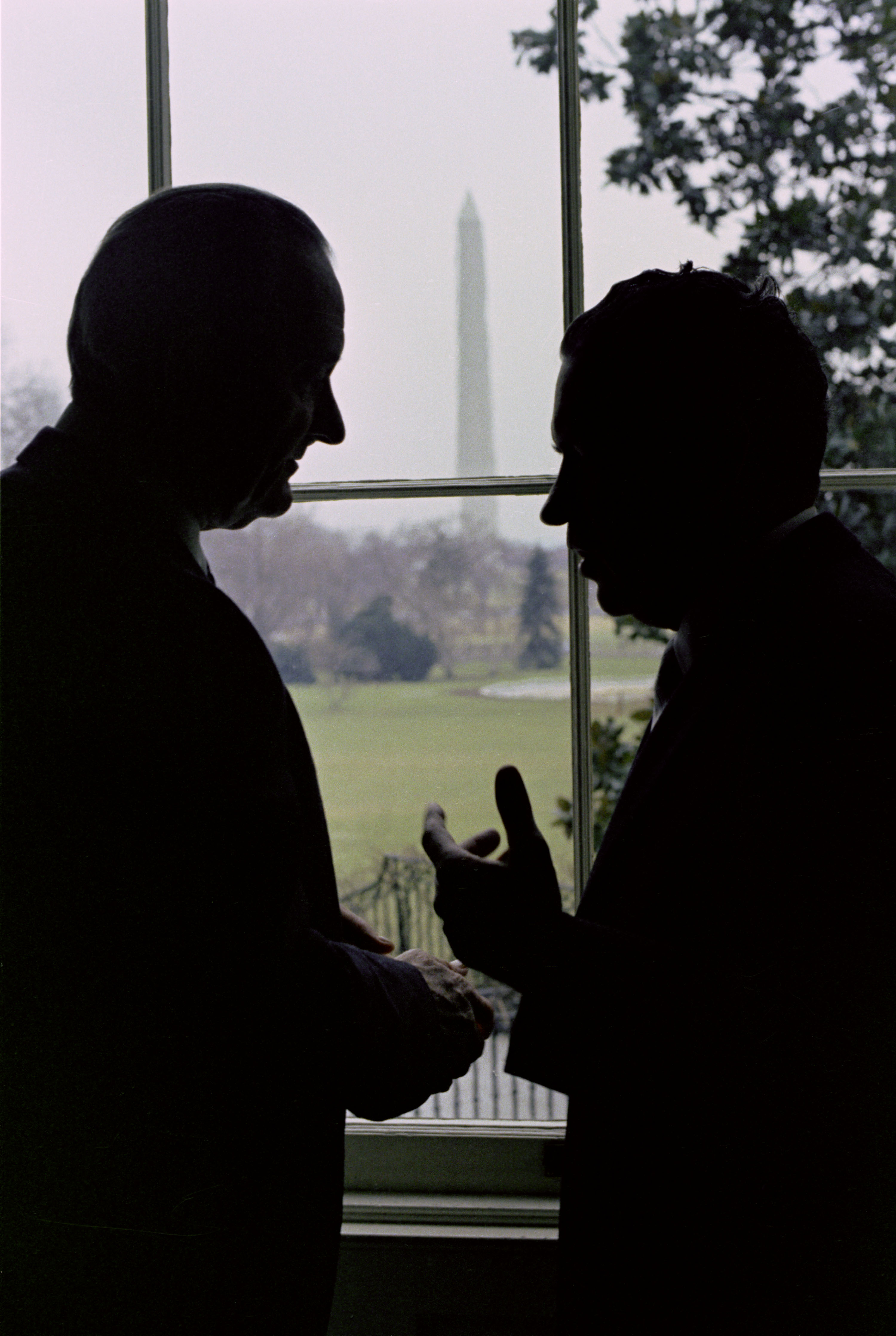 President Lyndon B. Johnson and President Richard Nixon in silhouette with the Washington Monument in the background.